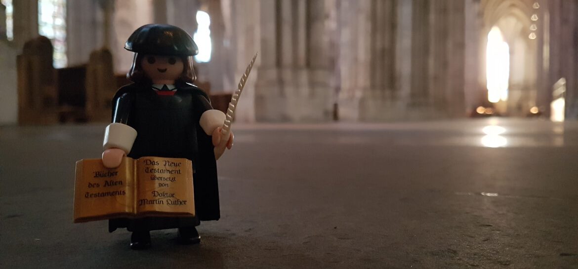 Der Playmobil Reformator Martin Luther im Kölner Dom. In den Händen hält er eine Bibel und eine Schreibfeder