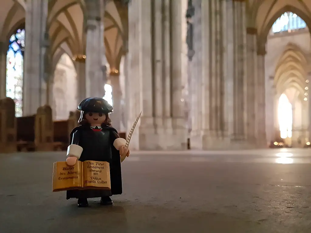 Der Playmobil Reformator Martin Luther im Kölner Dom. In den Händen hält er eine Bibel und eine Schreibfeder