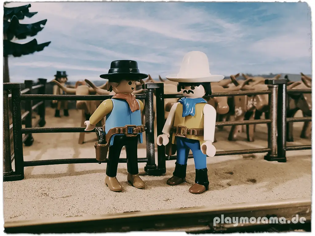 Vor der Western-Station sind Longhorn-Rinder in den Stallungen untergebracht, während zwei Playmobil Cowboys sich um sie kümmern und sich auf den bevorstehenden Viehtrieb vorbereiten.