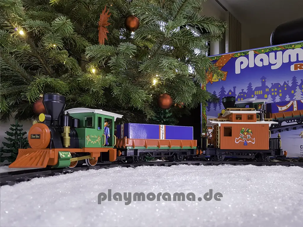 Festlicher Playmobil-Weihnachtszug vor dem Tannenbaum. Im Hintergrund ist die Originalverpackung (OVP) zu sehen.