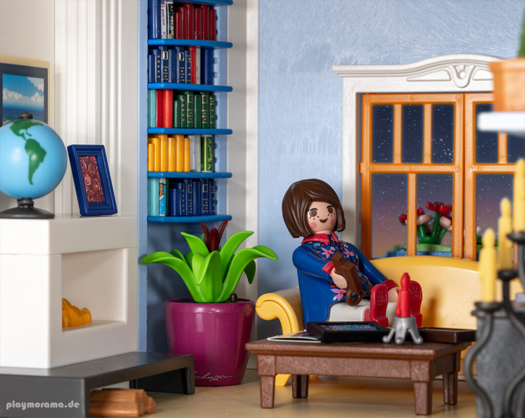 Playmobil Frau sitzt im Wohnzimmer mit Kamin entspannt auf der Couch und schaut auf den Fernseher.