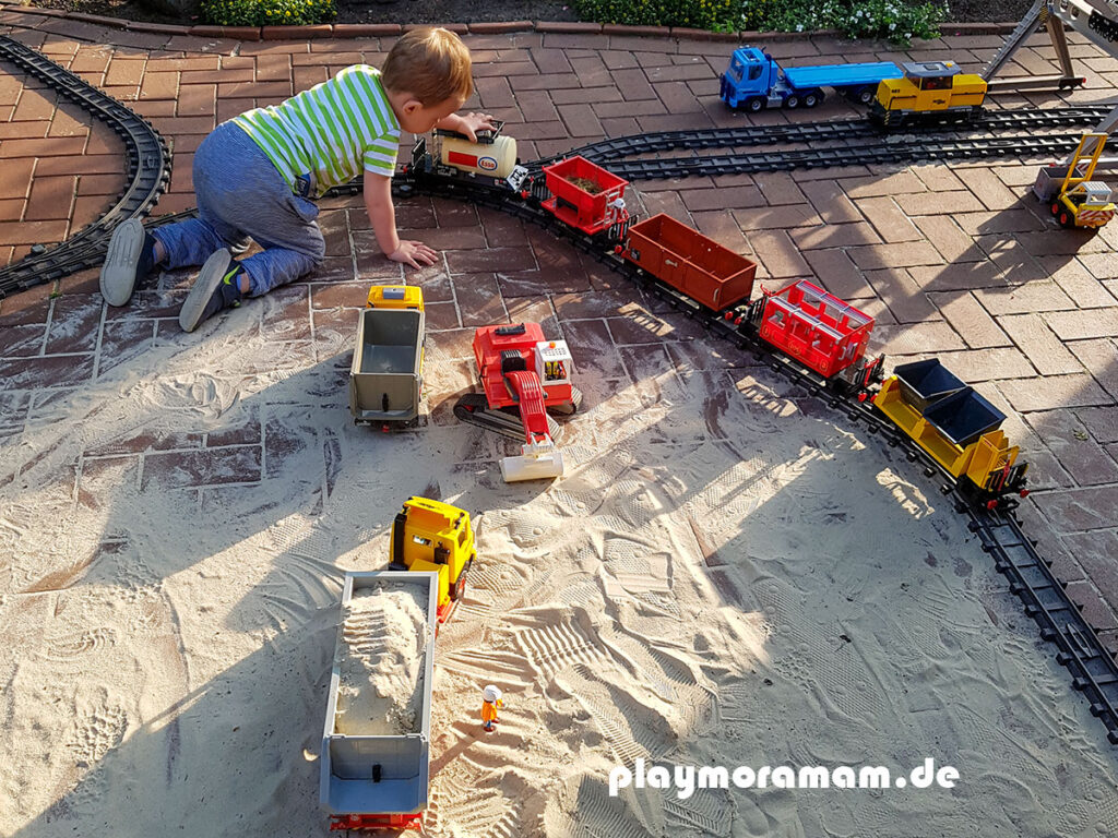 Kind spielt mit Playmobil Eisenbahn draußen im Garten