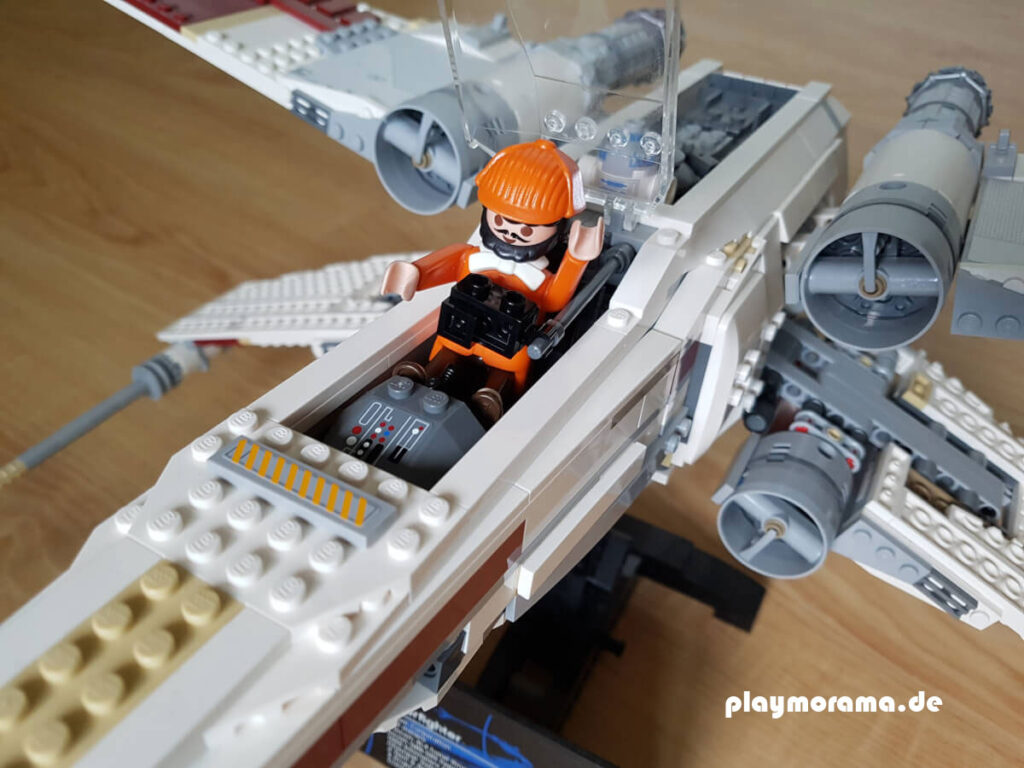 Playmobil Figur schaut sich einen Lego X-Wing 10240 an