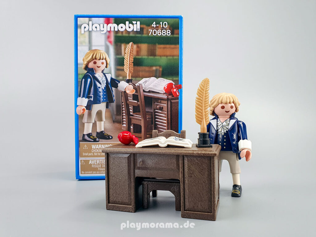 Die Playmobil-Sonderfigur zeigt ihn in historischem Gewand mit Schreibtisch, Schreibutensilien, Buch (Wilhelm Tell) und Apfel.