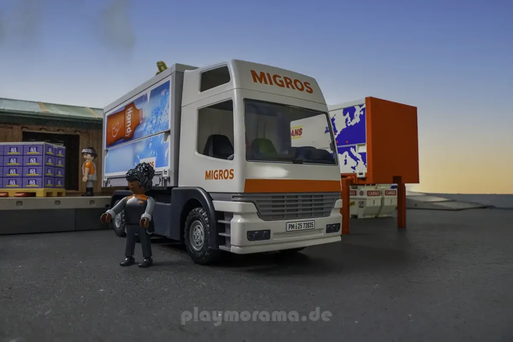 Migros-Fahrerfigur vor dem weißen PLAYMOBIL-LKW mit Ice-Tea-Palette auf der Laderampe im Hintergrund