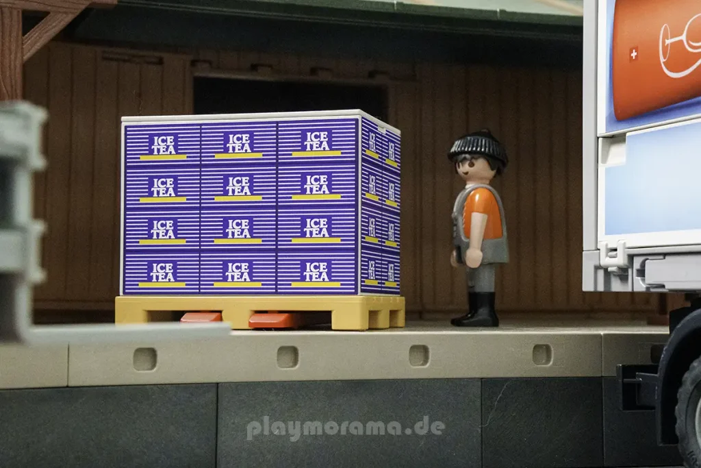 Palette mit blau beklebter Ice-Tea-Box auf der Laderampe neben einer PLAYMOBIL-Lagerfigur