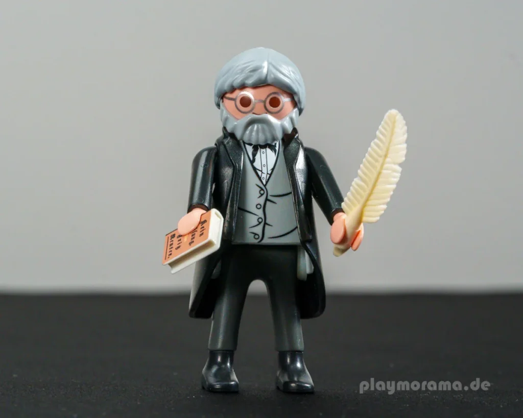 Playmobil hat Fritz Reuter mit historischer Kleidung und seinem charakteristischen Bart umgesetzt. Ein kleines Buch und eine Schreibfeder greifen seine Tätigkeit als Schriftsteller auf.