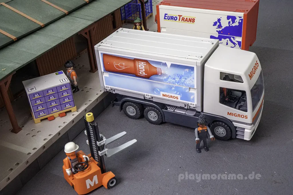 Orangefarbener Handstapler vor dem Migros-LKW an der Güterabfertigung, schräg von oben fotografiert