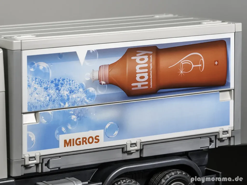Detail des Migros-Wechselkoffers mit roter Handy-Spülmittelflasche und Seifenblasen auf blauem Hintergrund